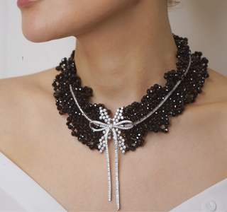 Black Onyx Bow Tie Necklace in sterling silver with lab sapphires, featuring a bow-shaped design and onyx center, displayed against a soft, neutral background