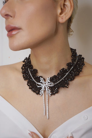 Black Onyx Bow Tie Necklace in sterling silver with lab sapphires, featuring a bow-shaped design and onyx center, displayed against a soft, neutral background