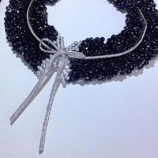 Black Onyx Bow Tie Necklace in sterling silver with lab sapphires, featuring a bow-shaped design and onyx center, displayed against a soft, neutral background