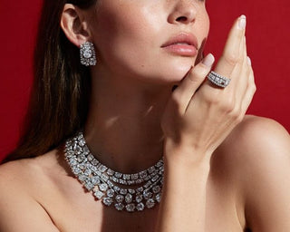 Close-up of a model wearing a layered diamond necklace with matching diamond earrings and a diamond ring in a luxury studio setting