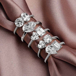 A luxurious collection of lab-grown diamond engagement rings in various cuts—including round, pear, emerald, heart, and cushion—set in white gold, elegantly displayed on a rose satin fabric.