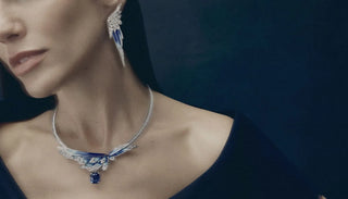 Elegant woman wearing a dramatic high jewellery necklace and matching earrings, featuring diamonds, blue enamel detailing and a suspended deep blue gemstone.