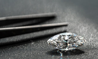 Loose marquise cut diamond on a black textured surface with jeweler's tweezers in the background, highlighting its shape and brilliance
