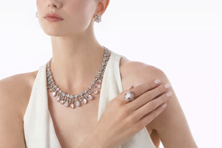 Woman wearing a blush pink gemstone necklace with matching stud earrings and a square cocktail ring in white gold
