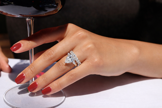 Close-up of hand wearing pear shaped diamond engagement ring with red manicure resting on a wine glass