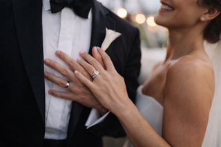 Intimate wedding portrait highlighting a diamond engagement ring on the bride’s hand placed on the groom’s chest, with soft lighting and blurred background.