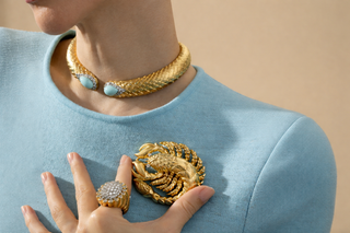 Model wearing a gold choker necklace with turquoise accents and a Scorpio-inspired gold brooch on a blue top
