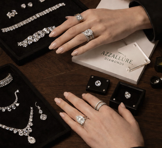 Luxury diamond jewelry consultation with hands wearing diamond rings, loose diamonds, tennis bracelets, and bespoke pieces displayed on black velvet trays at a wooden table