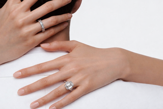 Close-up of a woman’s hands wearing a large emerald-cut diamond engagement ring and a baguette diamond eternity band against a soft white background.