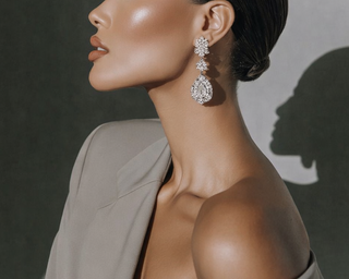 Elegant woman in profile wearing statement diamond drop earrings and a structured blazer with dramatic shadow lighting.
