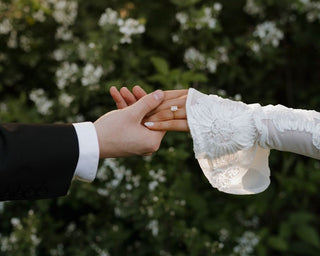 Couple holding hands outdoors showing a custom engagement ring on the bride’s finger