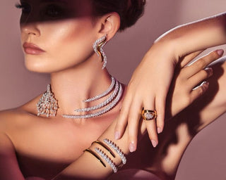 Model wearing diamond earrings layered diamond necklace gold cuff bracelets and a statement diamond ring styled in an editorial luxury photoshoot