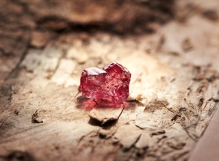 Close up of a vivid natural rough pink diamond resting on an earthy textured surface, highlighting its uncut form, natural inclusions and distinctive pink colour.